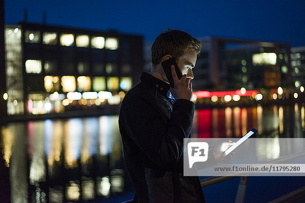 Junger Mann am Telefon schaut nachts auf die Tablette