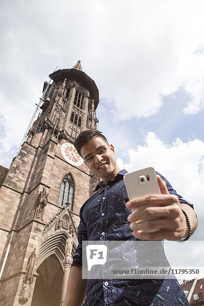 Deutschland  Freiburg  junger Mann  der einen Selfie an der Klosterkirche nimmt