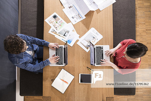 Overhead view of man and woman using laptops on table