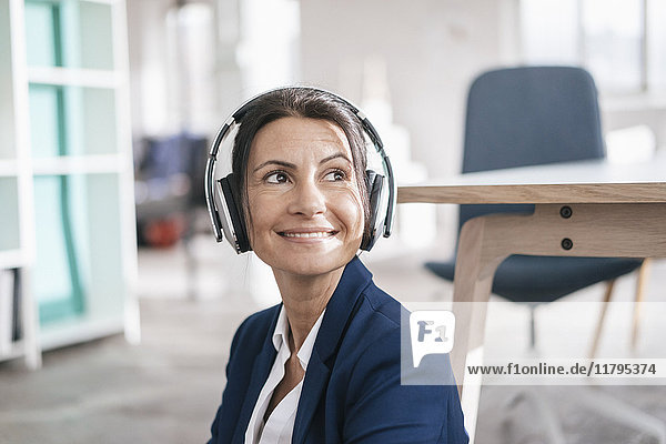 Porträt einer lächelnden Geschäftsfrau in einem Loft  die mit Kopfhörern Musik hört.