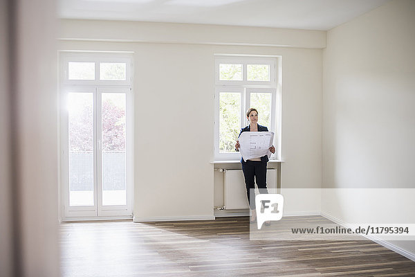 Woman in empty apartment with plan