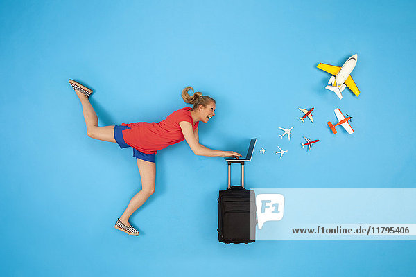 Woman with suitcase looking at laptop with airplanes coming out