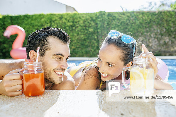 Happy couple in swimming pool with drinks at the poolside