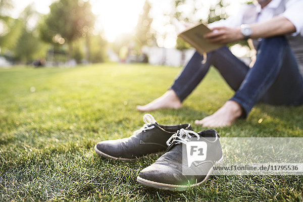 Unkenntlicher Geschäftsmann im Stadtpark auf Gras sitzend Lesebuch