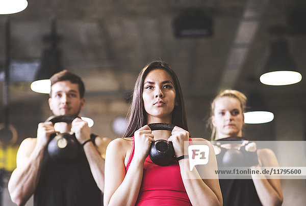 Confident young woman with training partners lifting kettlebell in gym
