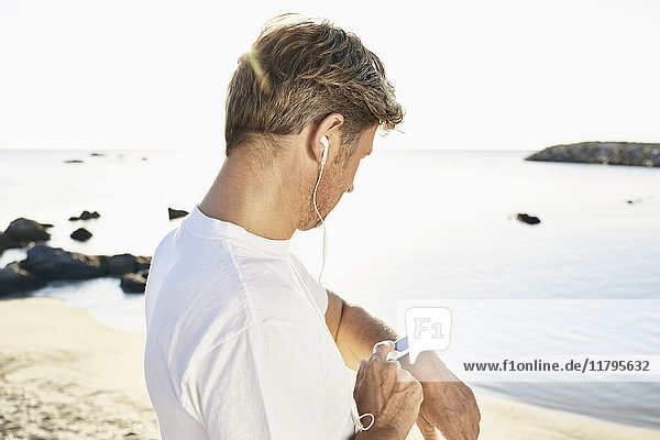 Erwachsener Mann mit Kopfhörer  der nach dem Joggen am Strand seine Smartwatch überprüft.