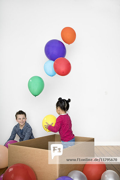 Zwei Kinder spielen mit Ballon und Pappschachtel