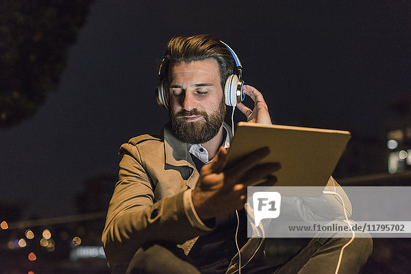 Young man with tablet and headphones in the city at night