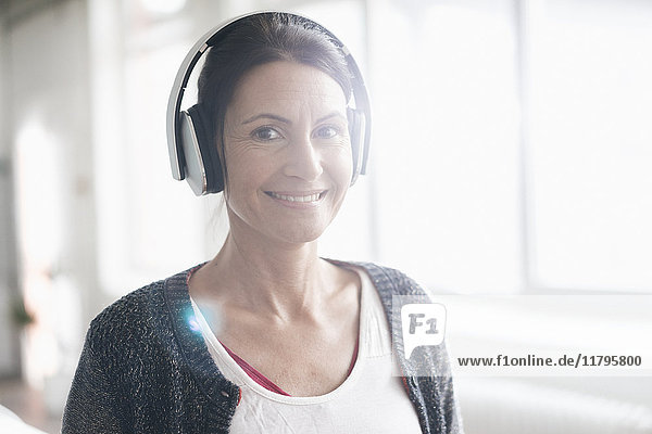 Porträt einer lächelnden Frau beim Musikhören mit Kopfhörern vor dem Fenster