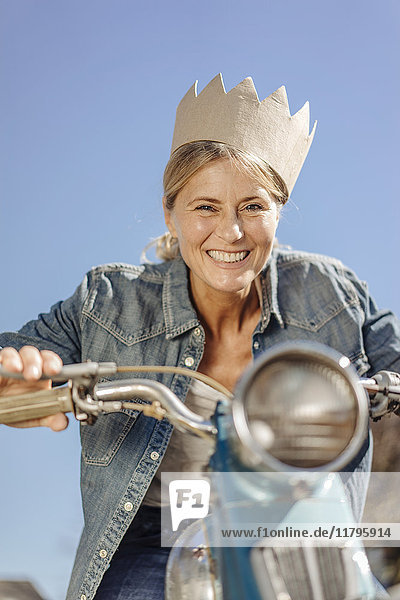 Smiling woman on vintage motorcycle wearing a crown