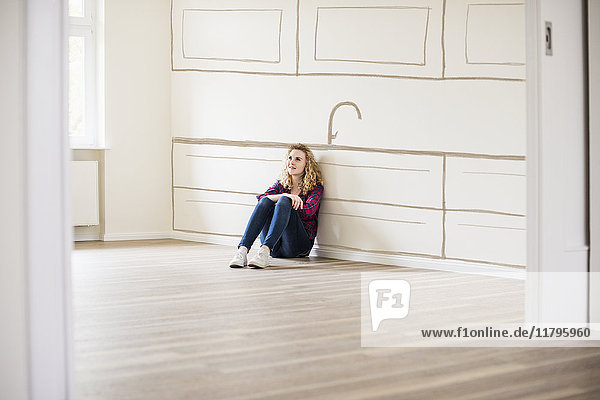 Junge Frau im neuen Zuhause sitzt auf dem Boden und denkt über Innenarchitektur nach.