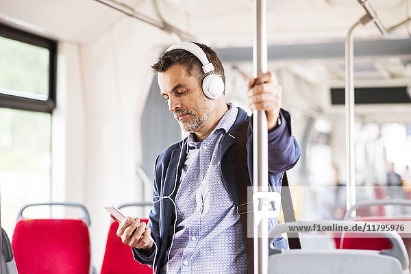 Businessman with smartphone and headphones travelling by bus