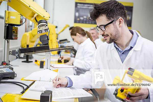 Engineer in factory holding model of an industrial robot taking notes on clipboard