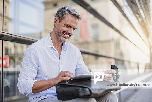 Smiling man sitting in the city using tablet