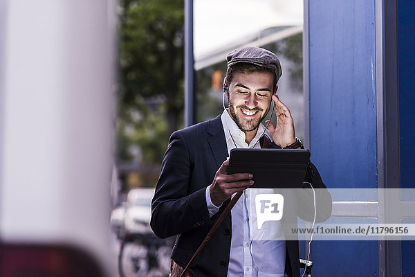 Smiling young man in the city with earphones and tablet