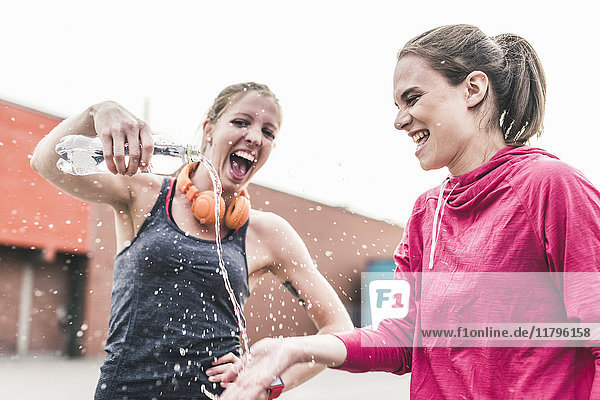 Zwei verspielte Frauen mit Wasserflasche  die eine Trainingspause einlegen.