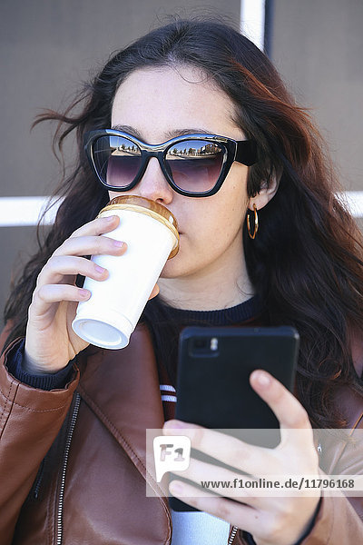 Portrait einer jungen Frau mit Kaffee zum Mitnehmen mit Smartphone