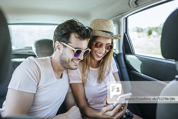 Couple in the back seat of a car looking at a cell phone