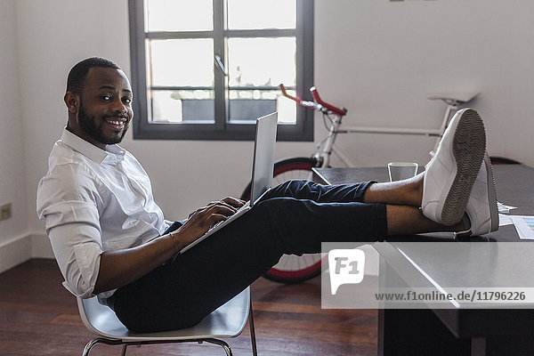 Man using laptop in home office with feet on desk