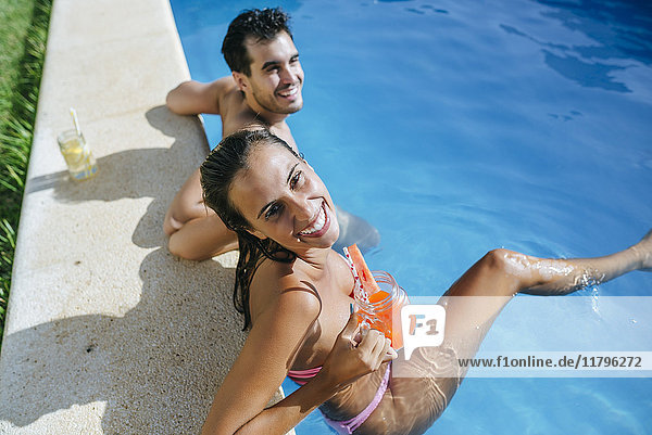 Happy couple in swimming pool with drink at the poolside