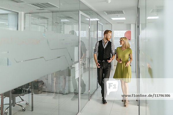 Geschäftsmann und Frau  die im Büroflur spazieren gehen und reden