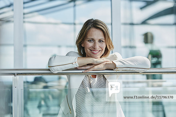 Porträt einer lächelnden Geschäftsfrau  die sich auf das Geländer am Flughafen stützt.