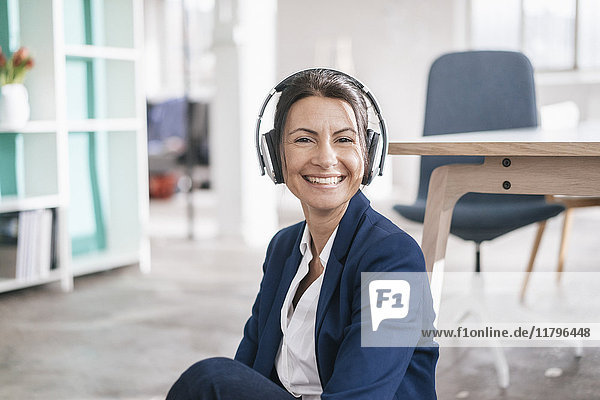 Portrait of happy businesswoman in a loft listening music with headphones