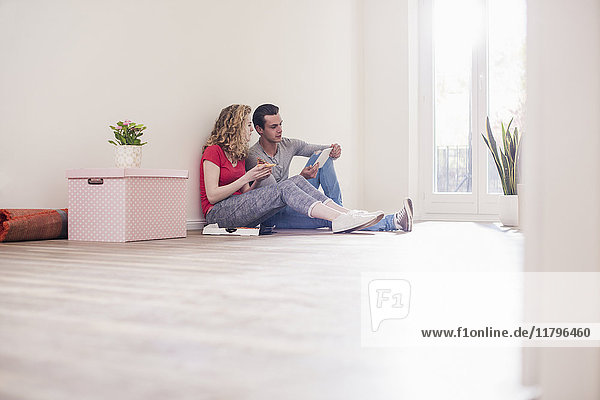 Junges Paar in neuem Zuhause sitzend auf dem Boden mit Tablette