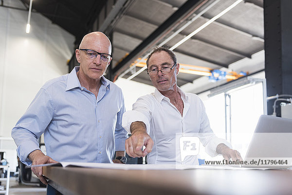 Two businessmen looking at plan on table in factory