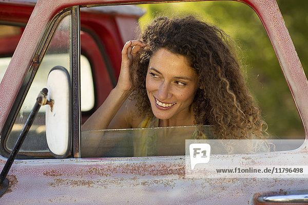 Happy young woman fixing her hair in car miror
