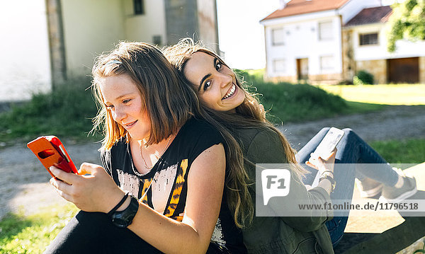 Zwei glückliche Mädchen mit ihren Smartphones im Freien