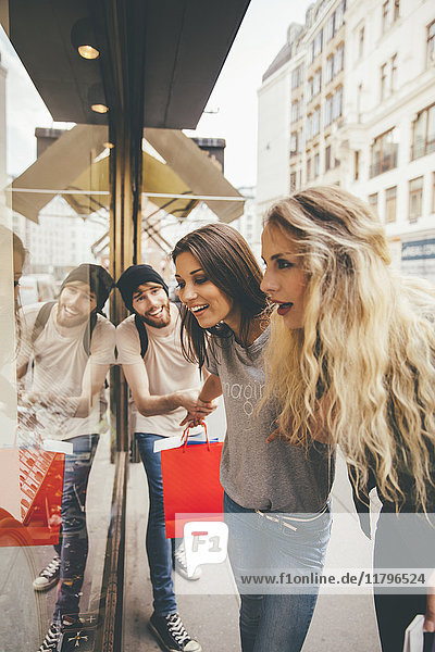 Young women looking fascinated in shop window  boyfriend trying to pull her away