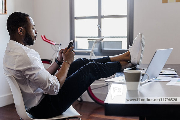 Man using cell phone in home office with feet on desk