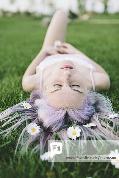Frau auf Gras liegend mit Blumen auf Haaren