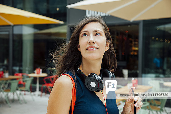 Porträt einer lächelnden jungen Frau mit Kopfhörer und Getränk zum Mitnehmen in der Stadt