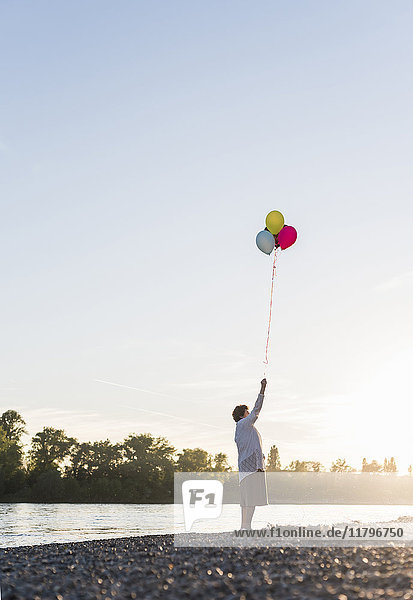 Seniorin mit Luftballons am Strand bei Sonnenuntergang