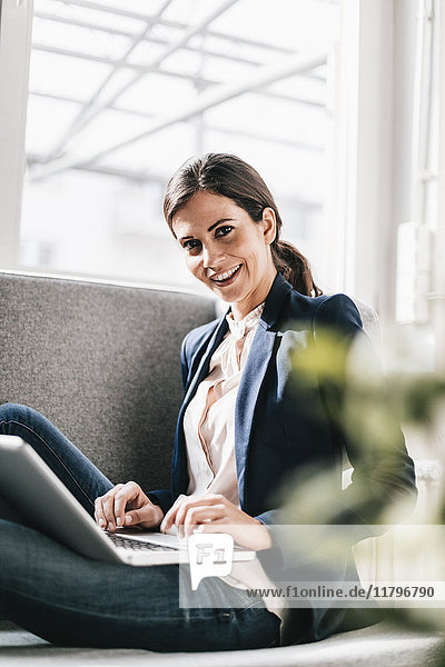 Portrait einer lächelnden Geschäftsfrau mit Laptop auf der Couch