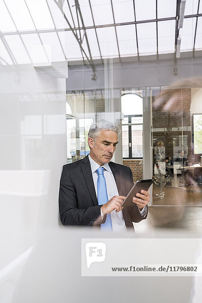 Mature businessman sitting in office  using digital tablet