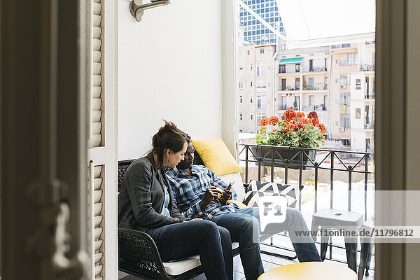 Two young professionals on office balcony  using their smartphones