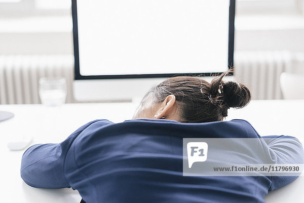 Back view of overworked woman sleeping on desk in office