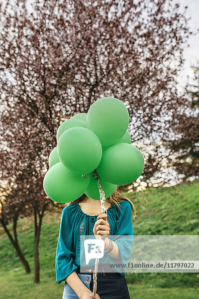 Junge Frau versteckt sich hinter grünen Luftballons