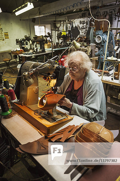 Ältere Frau sitzt an einer Nähmaschine in einer Schusterwerkstatt.