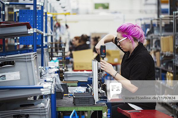 A young woman with pink hair using a power tool on a cycle frame. A skilled factory worker assembling a bicycle in a factory.