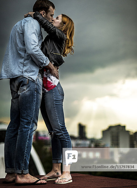 A couple standing and kissing on a city rooftop.