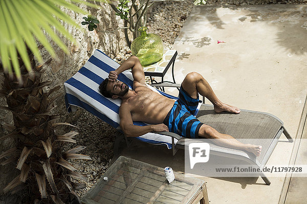 Hochwinkelaufnahme eines Mannes in Badehose  der auf einer Sonnenliege liegt.