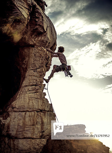 Bergsteiger  der eine Felsformation in einer gebirgigen Landschaft besteigt.