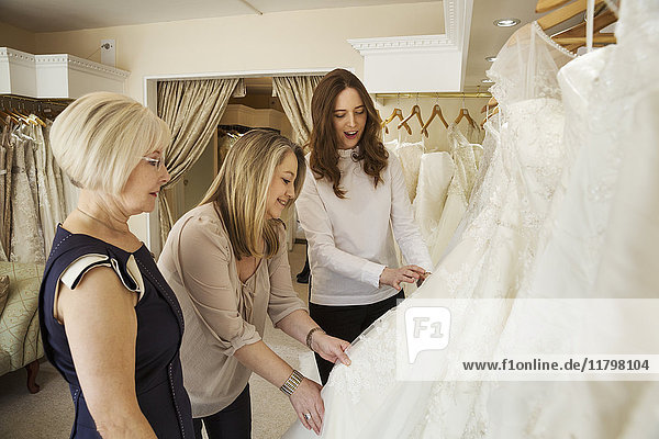 Drei Frauen  eine Kundin und zwei Einzelhandelsberaterinnen in einem Brautkleidergeschäft  die die Auswahl der Kleider durchsehen.
