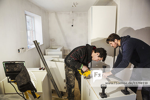 Zwei Bauarbeiter  die mit einer Kreissäge Gipskartonplatten für eine Küchenzeile zuschneiden.