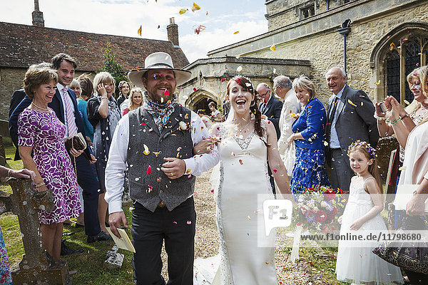 Lächelndes Brautpaar verlässt die Kirche  ein Gast wirft Konfetti.