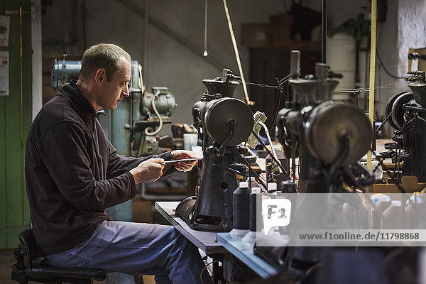 Man sitting at a sewing machine in a shoemaker's workshop.